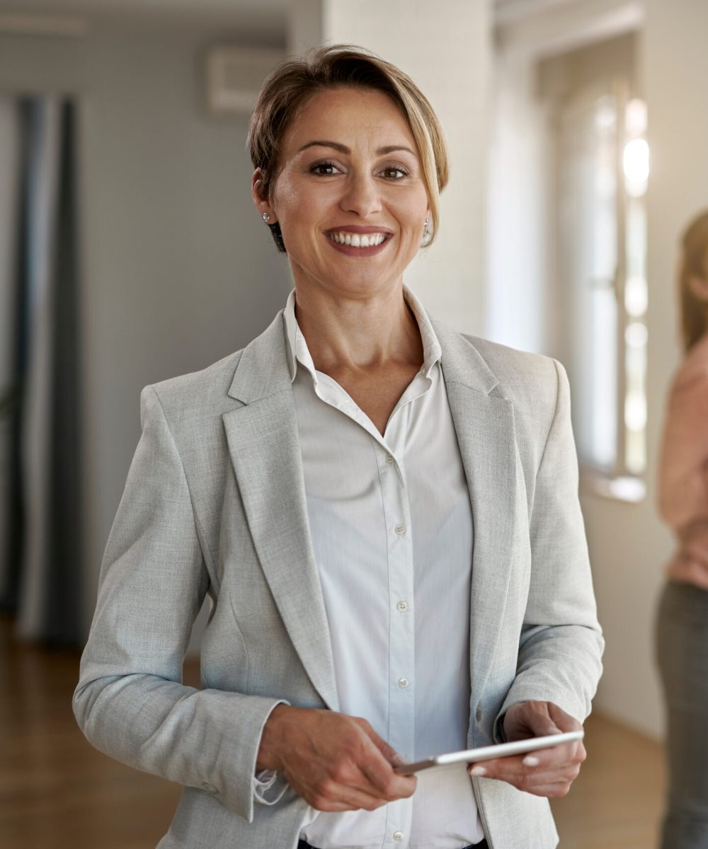 Portrait of happy real estate agent looking at the camera while her clients are standing in the background.