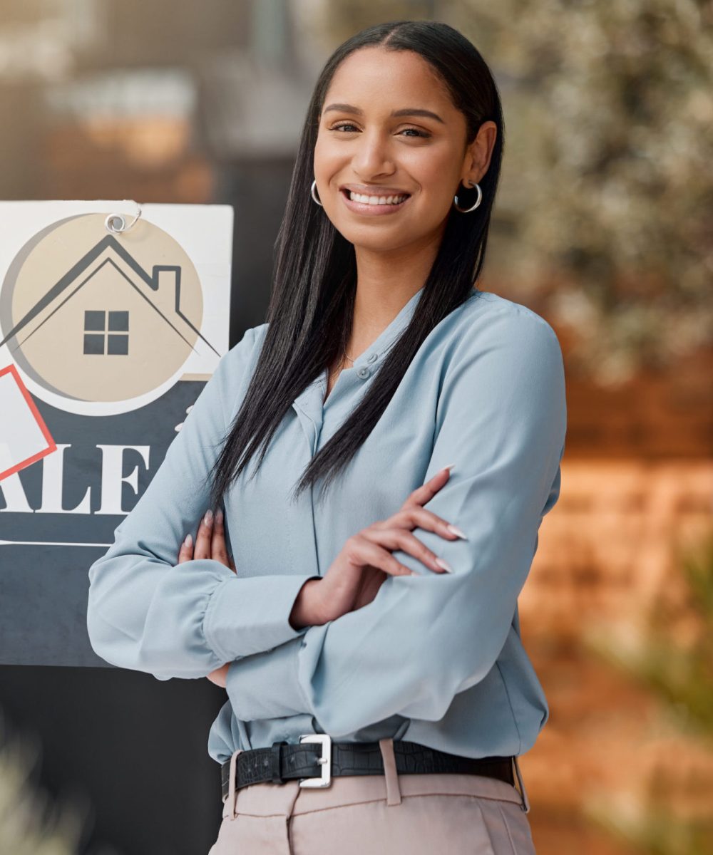 Shot of a real estate agent standing next to a sold sign outside.